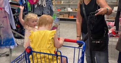 Long blond-haired woman with two young blonde children, each dressed in yellow, shopping for clothing