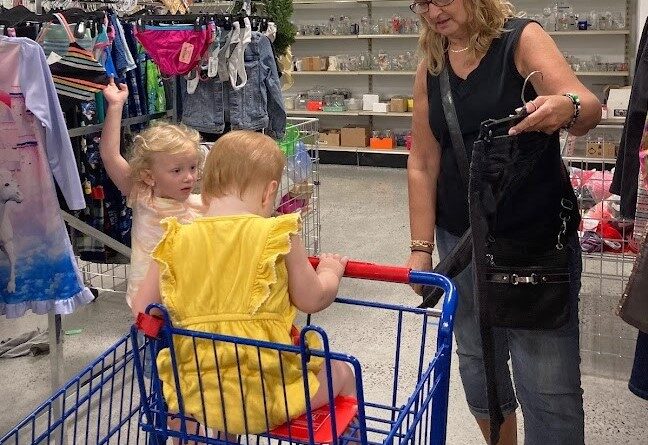 Long blond-haired woman with two young blonde children, each dressed in yellow, shopping for clothing