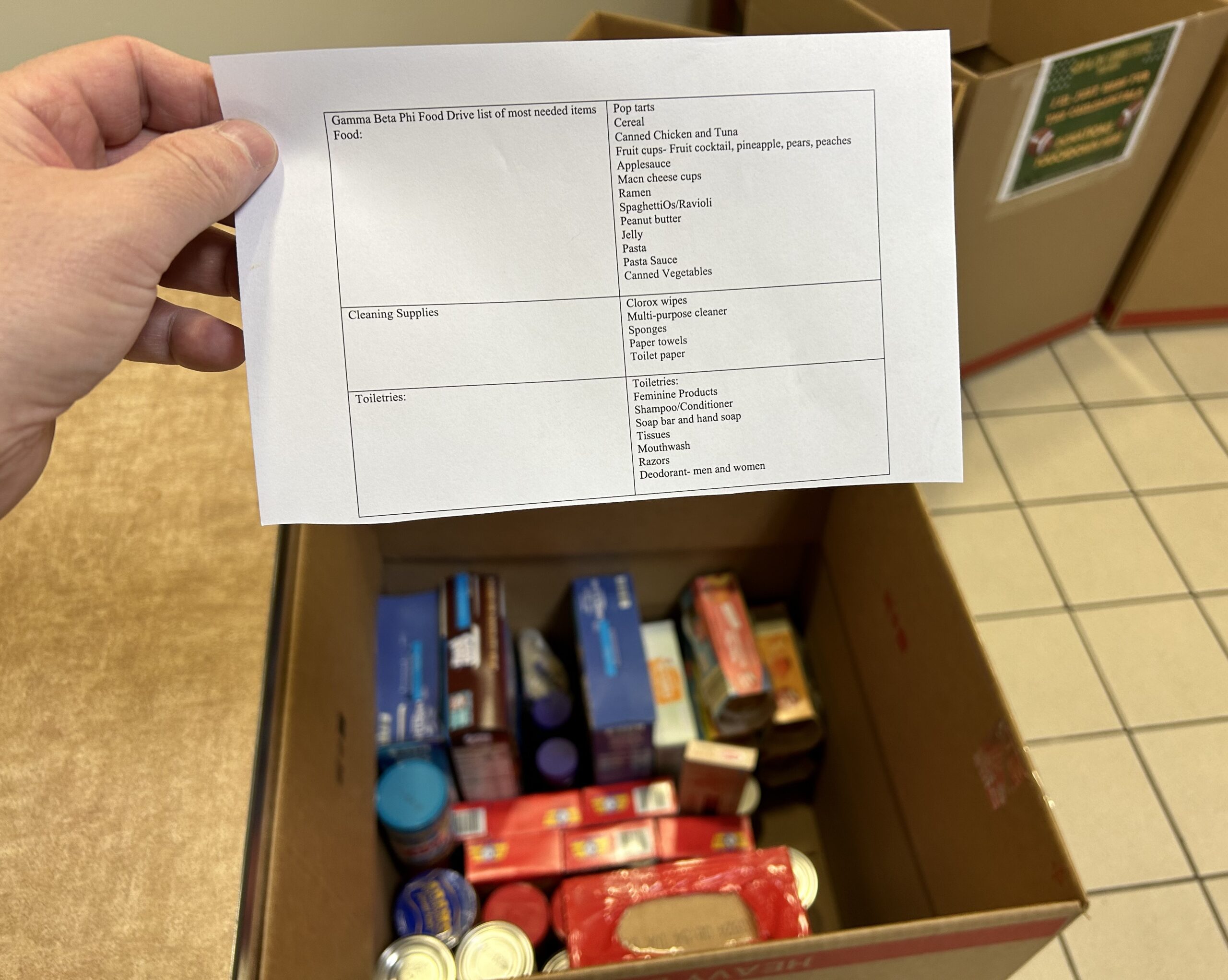 Hand holding a white paper form with a list of items to donate to the campus food pantry