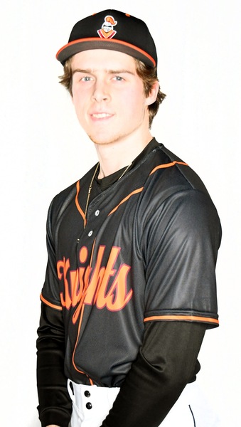 Young man with chin beard in baseball uniform, black jersey with orange "Knights" in script and and orange low neck and short sleeve-shirt trim, with black baseball cap with orange on the brim edge and an orange and maroon knight logo on the front, middle.