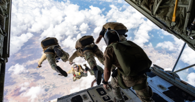 Three U.S. paratroopers jumping out of a plane into a sky of clouds against a blue sky