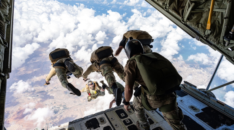 Three U.S. paratroopers jumping out of a plane into a sky of clouds against a blue sky