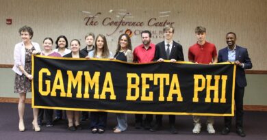 Eleven men and women standing behind a black banner they're holding with Gamma Beta Phi in gold letters on the front