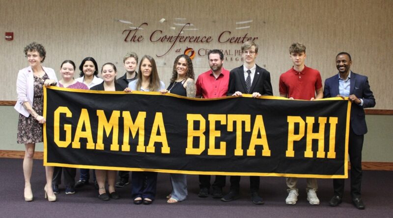Eleven men and women standing behind a black banner they're holding with Gamma Beta Phi in gold letters on the front