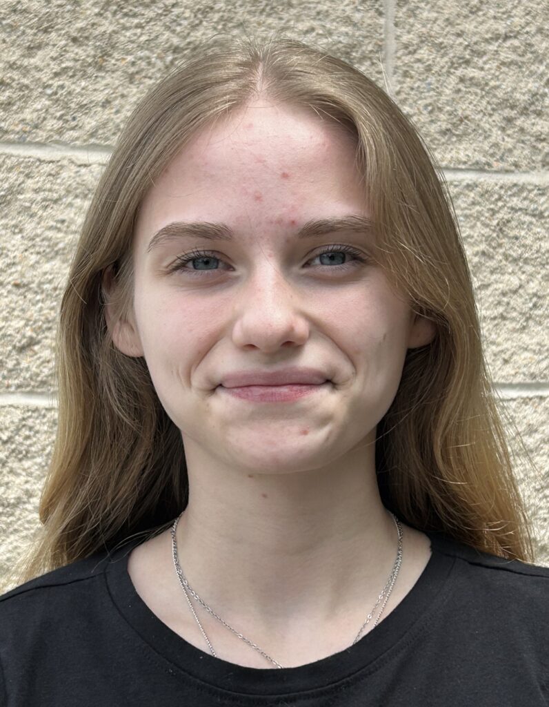 Young smiling woman with long blond hair and wearing a black collarless shirt. Jules Quare.