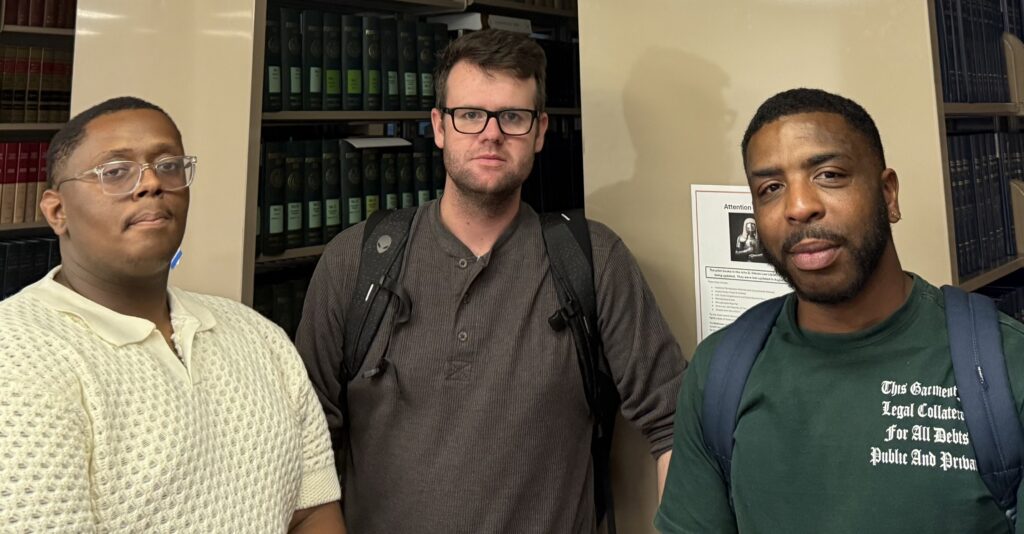 Photo of three young men standing in the front of bookshelves in a law library. From left, Seth Parr, Jared Gander and Arsenio Humphrey.