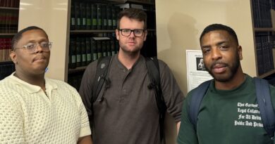 Three young men standing in front of the end of bookshelf rows in the Central Penn College Law Library. They are members of the school's debate team. From left, Seth Parr, Jared Gander and Arsenio Humphrey,