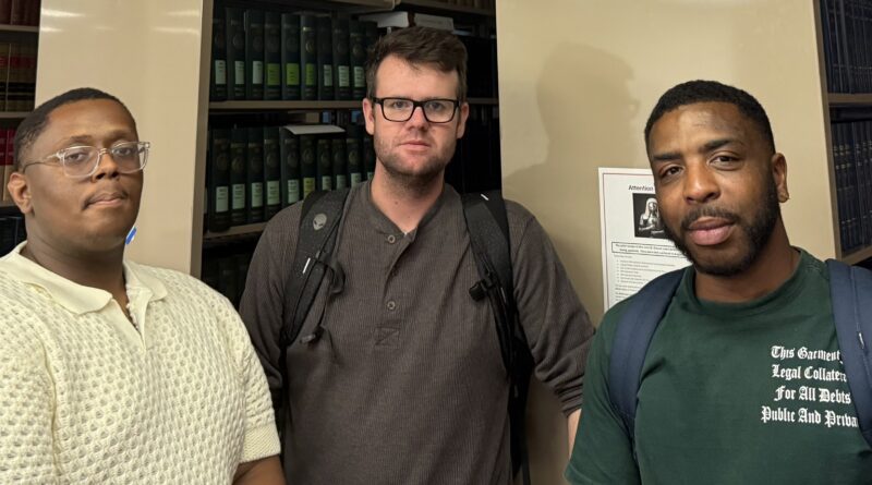 Three young men standing in front of the end of bookshelf rows in the Central Penn College Law Library. They are members of the school's debate team. From left, Seth Parr, Jared Gander and Arsenio Humphrey,