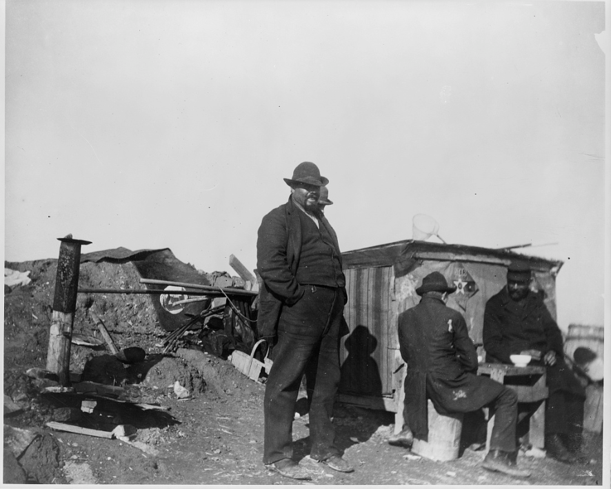 Grimy men in late-19th century garb around a small shanty and stove, during the Pullman Strike, in or near Chicago.