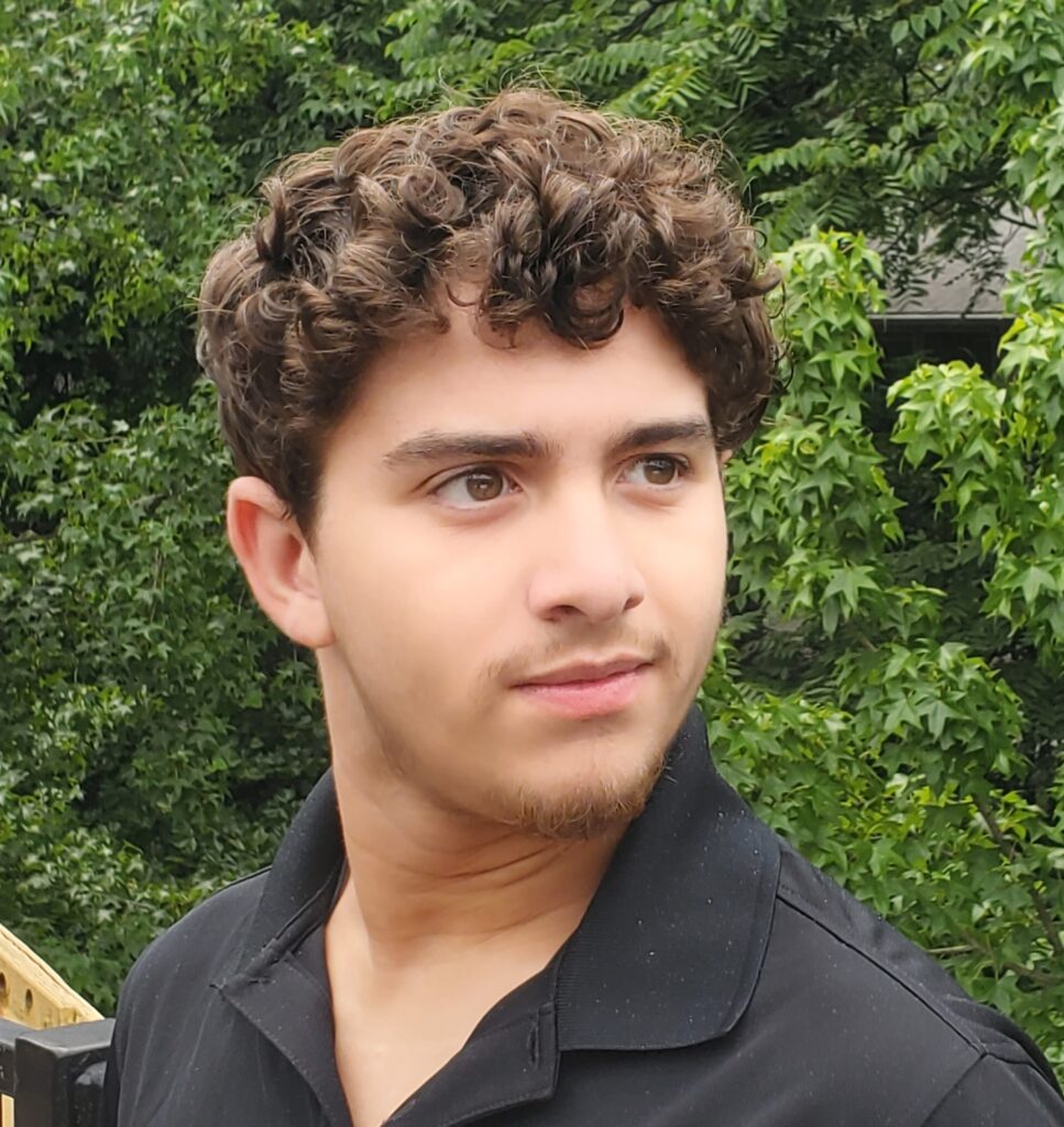 Young man with short curly hair and a serious, pensive expression, wearing a black polo shirt., Noah Lopez.