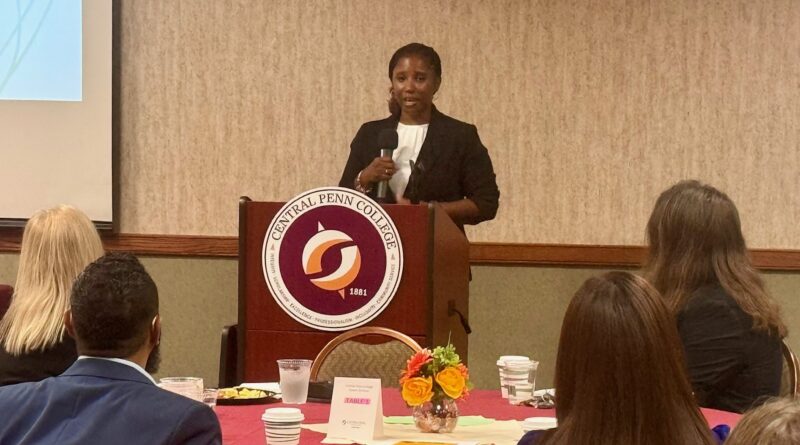 Wpoman in business attire at Central Penn College podium addressing a ballroom of people in the college's conference center during the 2025 Business Partner of the Year. Kim Craig