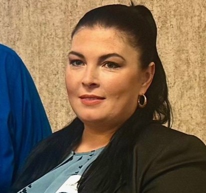 Woman with pinned-back long black hair and wearing a black blazer and gray blouse. Rosanna Wakley.