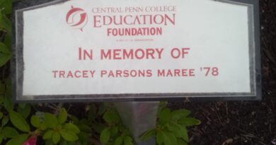 Small memorial plaque that is horizontally rectangular, with the upper border curved gently up in the middle. It has a white background and a gray border. In the middle, in red letters and numbers, is Central Penn College Education Foundation In Memory Of Tracey Parsons Maree '78.