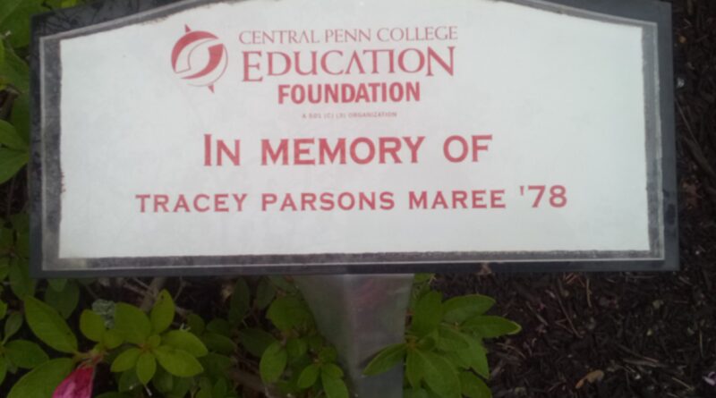 Small memorial plaque that is horizontally rectangular, with the upper border curved gently up in the middle. It has a white background and a gray border. In the middle, in red letters and numbers, is Central Penn College Education Foundation In Memory Of Tracey Parsons Maree '78.