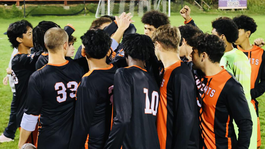 Young men in black-and-orange jerseys in a tight huddle, their hands up. The Central Penn Knights men's soccer team.