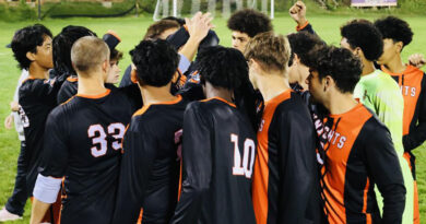 A group of young men in black and orange jerseys in a tight huddle, their hands up. Central Penn Knights men's soccer team.