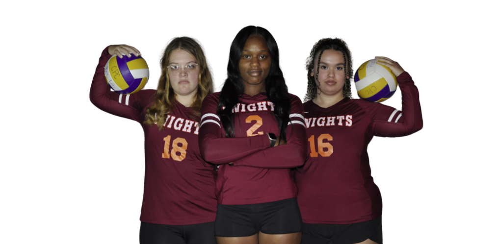Three young women in maroon long-sleeved volleyball jerseys with orange numbers on the, and KNIGHTS in white above the numbers. Women on the ends are holding a volleyball on their shoulder.