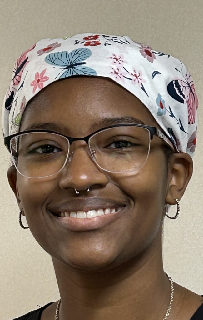 Smiling young woman wearing a white flower-patterned surgical cap.