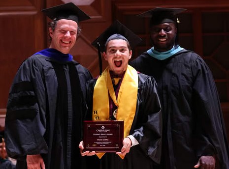 sSudent smiling mouth open, and standing between two men. All of the are wearing academic-graduation regalia. The student is Noah Lopez. The man on the left of the photo is Central Penn College Associate Provost Jared Rife, and the man on the right is Central Penn College Vice President of Student Services Romeo Azondekon. 2026 Central Penn graduation, at The Forum, in Harrisburg, Pennsylvania.