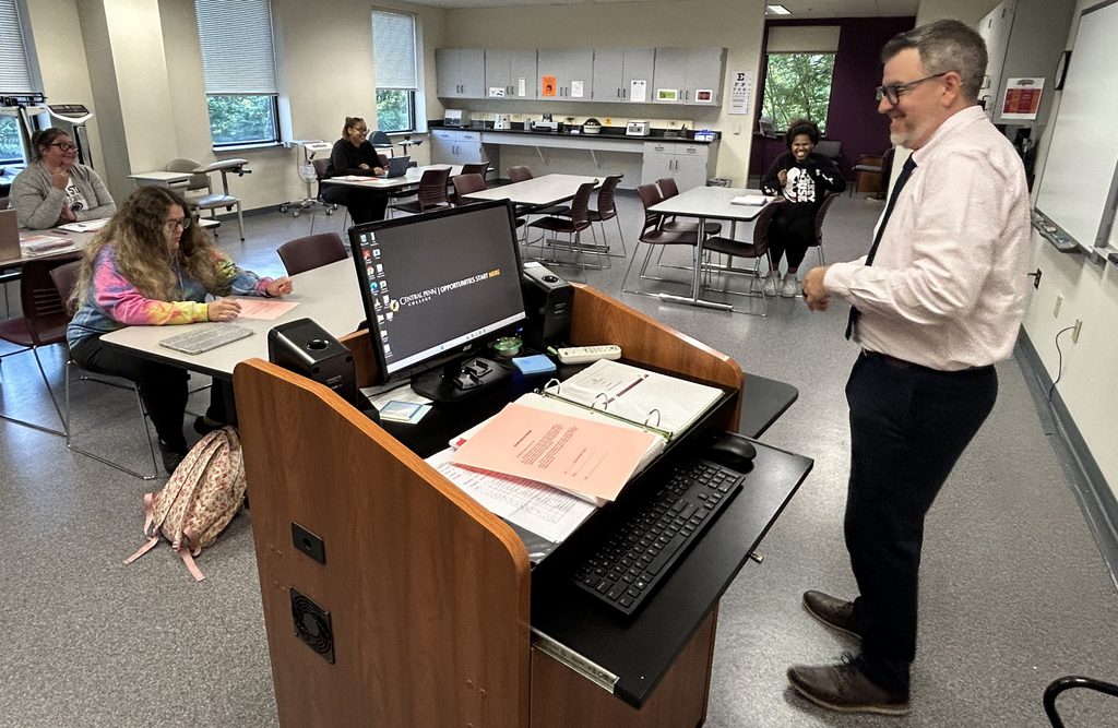 Four students at tables as Professor Christopher Adams talks to them before class in the Central Penn College medical-assisting lab.