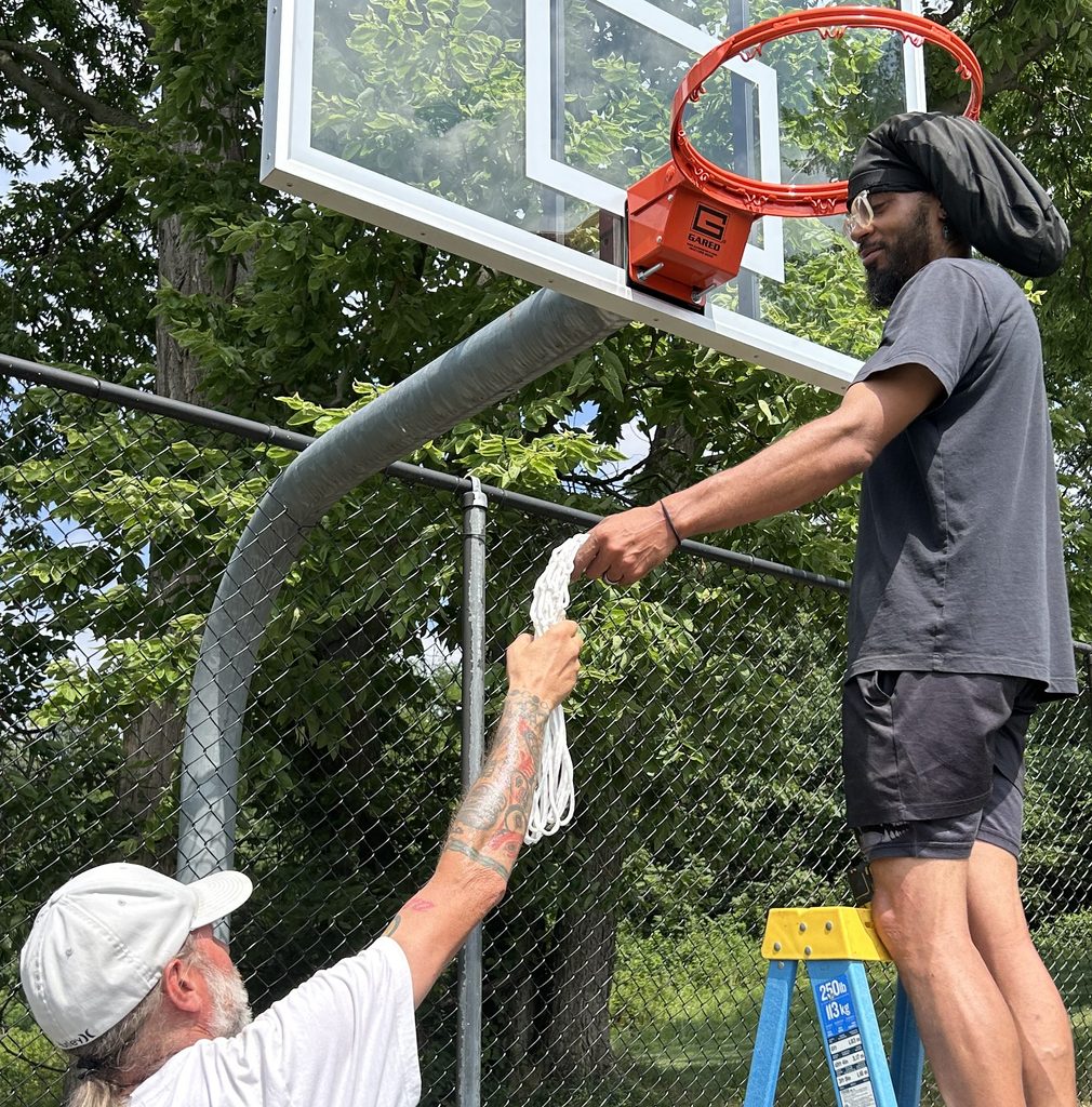 James Wilson hands Charles Milburne a net for the hoop on one of the new basketball backboards for the upper court of the two at the back of campus. Both courts got new backboards.