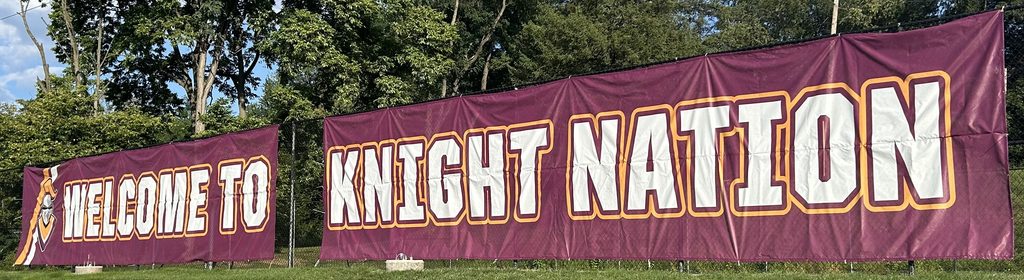 A maroon banner covers nearly the entire outside portion of the campus-facing  chain-link fence that surrounds the upper of the two basketball courts on the back of the Central Penn College campus. Welcome to Knight Nation is printed in wide white letters, each  surrounded by light-orange letters. On the right end of the banner, next to "Welcome," are a bright-orange and a white diagonal stripe, very close together, with an orange-and-silver image of a knight's helmet. "The Knights" is the demonym for the school's students, and is applied to its sports teams and culture. A medieval-style knight, Sir Will, is the Central Penn College mascot. Maroon and orange are the college's colors.