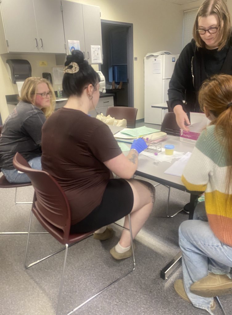 Phlebotomy -certificate students, sitting, from left, Chloey Freundel, Hannah Rumbel and Saroeun Cohenour, and standing, medical-assisting student Emily Anderson, test blood samples in the medical-assisting lab. Photo by Jules Quare